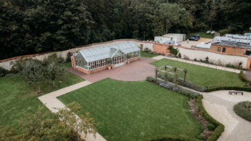Uma vista aérea de uma casa cercada por um jardim exuberante, com gramado verdejante e diversas plantas, destacando-se em meio à natureza ao ar livre.