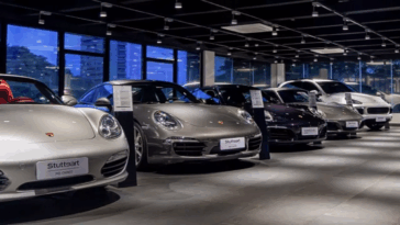 Um carro vermelho estacionado em frente a uma concessionária de veículos iluminada por lâmpadas ao anoitecer.